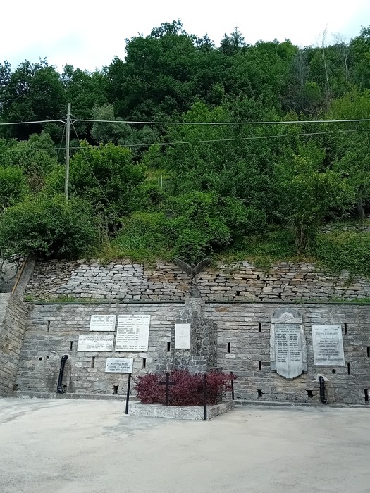 Monumento ai caduti circondato da vegetazione, con lastre commemorative incastonate nella pietra.