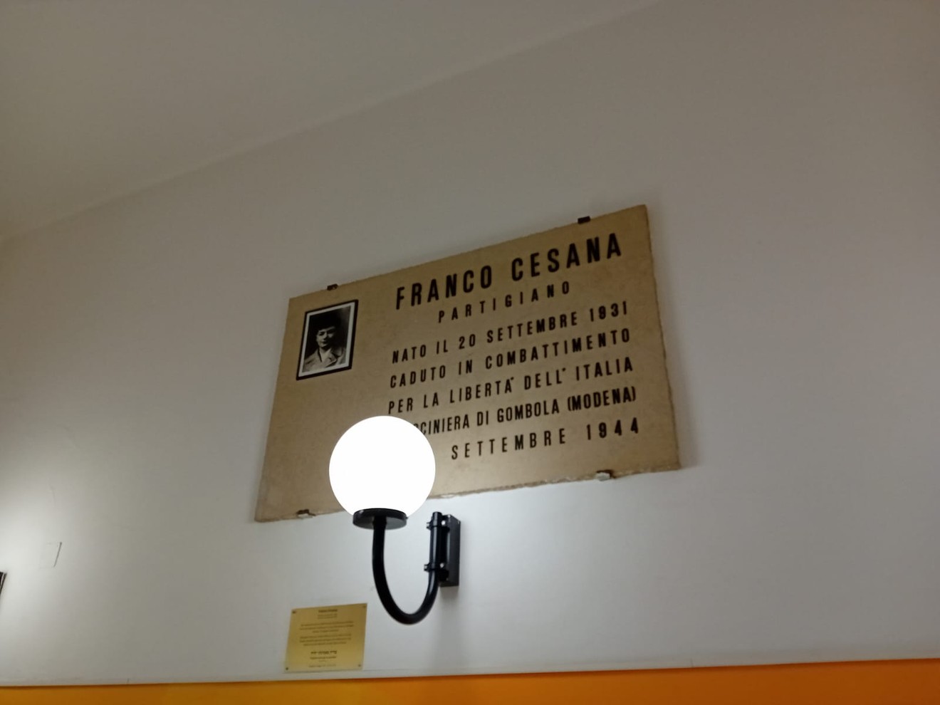 Lapide commemorativa dedicata a Franco Cesana, partigiano, collocata in un ambiente interno.