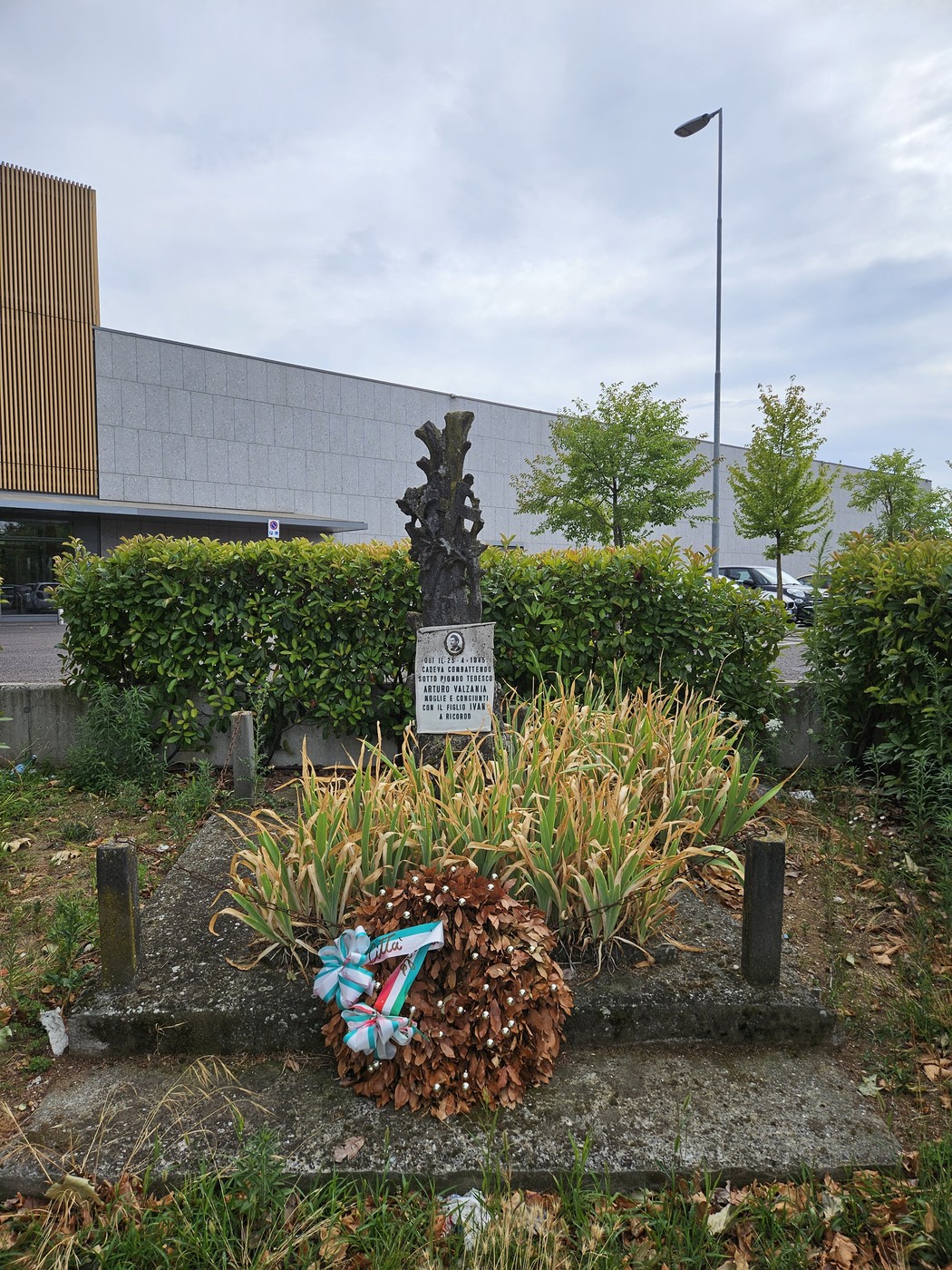 Cippo commemorativo a Valzania, circondato da piante, con una corona d'alloro ai piedi della stele.