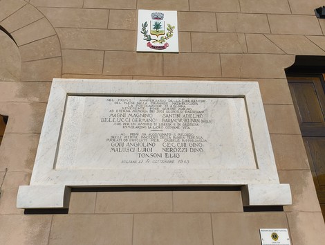 Lapide commemorativa per il primo anniversario di un evento, scolpita in marmo con simboli e nomi.