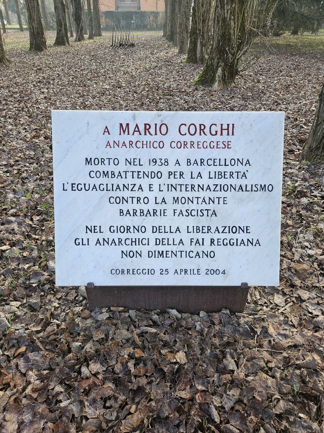 Lapide commemorativa a Mario Corghi, anarchico, situata in un ambiente boschivo.