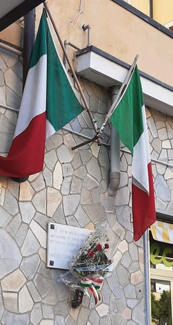 Lapide commemorativa dedicata a Costelli e Canelli, decorata con fiori e bandiere italiane.