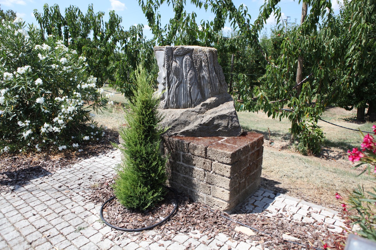 Monumento ai Caduti della Libertà circondato da un giardino, con rilievi sulle pareti e vegetazione verde.