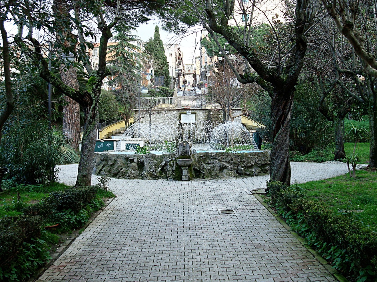 Lapide commemorativa di Enriquez Agnoletti in un giardino con fontana e alberi.