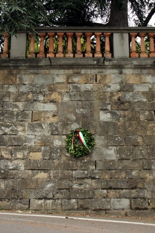 Lapide storica a Giugni, con corona d'alloro e nastro tricolore su un muro in pietra.