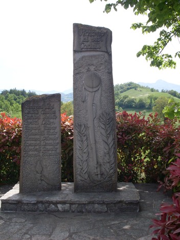 Monumento ai Caduti di Rosano, dedicato ai combattenti, circondato da vegetazione e montagne sullo sfondo.