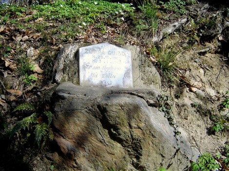 Lapide commemorativa su una roccia, incastonata nella natura, con una scritta su fondo chiaro.