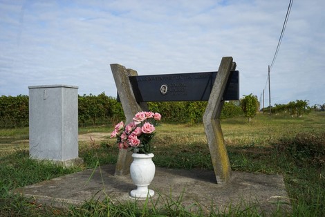 Monumento a Caiumi con fiori, situato in un paesaggio aperto e verdeggiante.