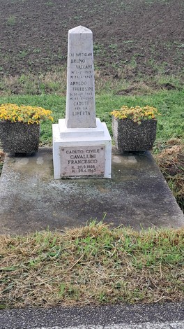 Cippo commemorativo dedicato a Vaccari, Tredesini e Cavallini, con aiuole di fiori gialli circostanti.