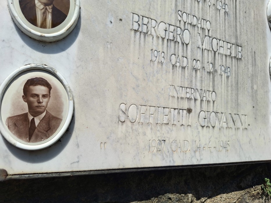 Lapide commemorativa con fotografie e nomi di caduti in guerra, decorata con simboli di memoria.