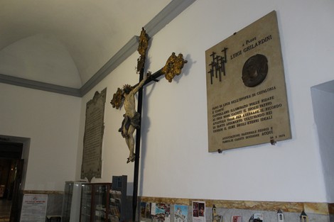 Lapide commemorativa a Ghilardini, affiancata da una croce con Cristo, in un ambiente storico.