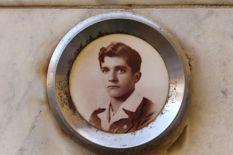 Lapide commemorativa con foto in ceramica di un giovane uomo su fondo di marmo.