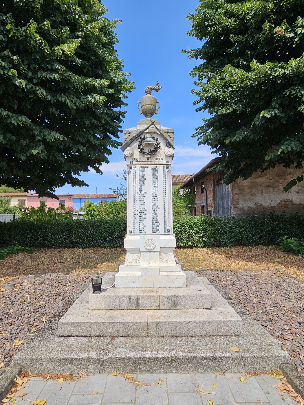 Monumento ai Caduti di Corno Giovine, con pregiata scultura e nomi incisi, contornato da alberi e un cielo sereno.