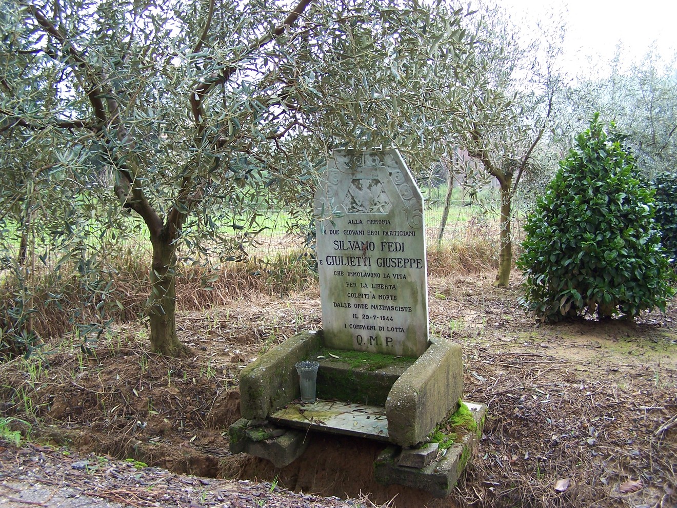 Cippo commemorativo dedicato a Silvano Fedi e Giulietti Giuseppe, immerso nel verde degli ulivi.