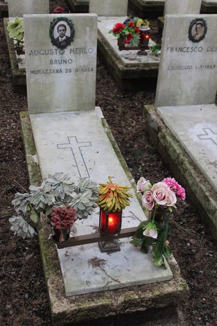 Tombe commemorative con fiori e candele, dedicate ai caduti per la Libertà. Atmosfera di rispetto e memoria.