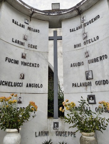 Sacrario dei deportati con monumento in marmo e foto commemorative, adornato da fiori.