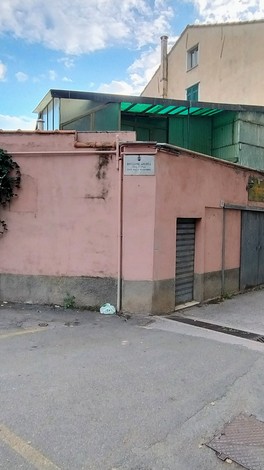 Lapide commemorativa a Bruzzone su un edificio rosa, con un retro in cemento e una struttura moderna sopra.