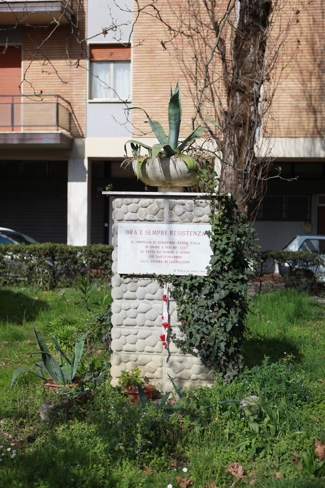 Lapide commemorativa dedicata agli uomini e alle donne della Resistenza, circondata da vegetazione.
