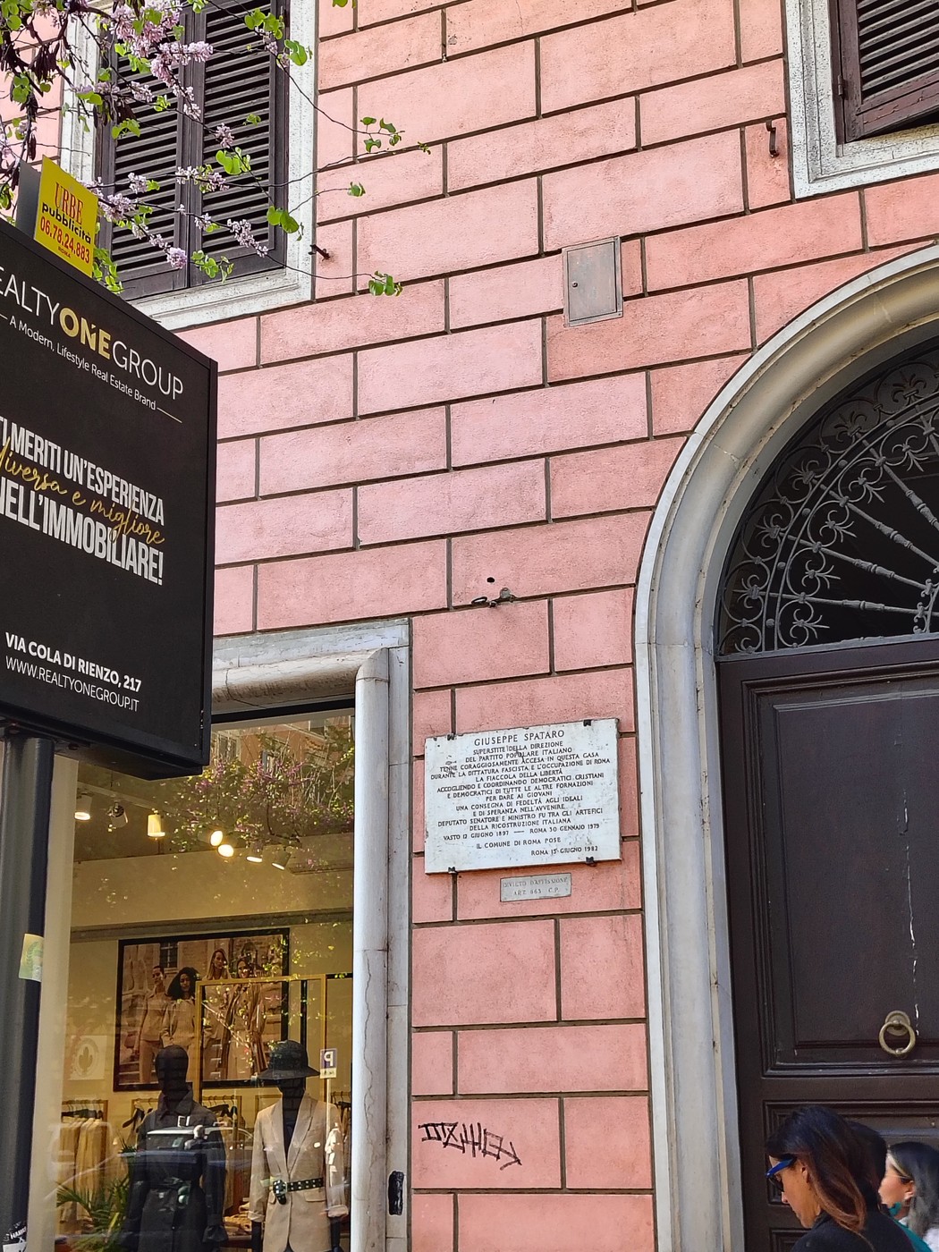 Lapide commemorativa a Spataro su una parete di un edificio storico, con dettagli architettonici e fiori in primo piano.