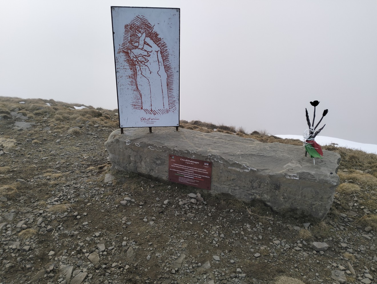 Monumento al "Fiore del partigiano" su una roccia, con un'immagine simbolica e una decorazione floreale.
