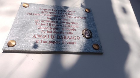Lapide commemorativa dedicata a Angelo Barzago, incisa su pietra, con elementi decorativi e scritte significative.
