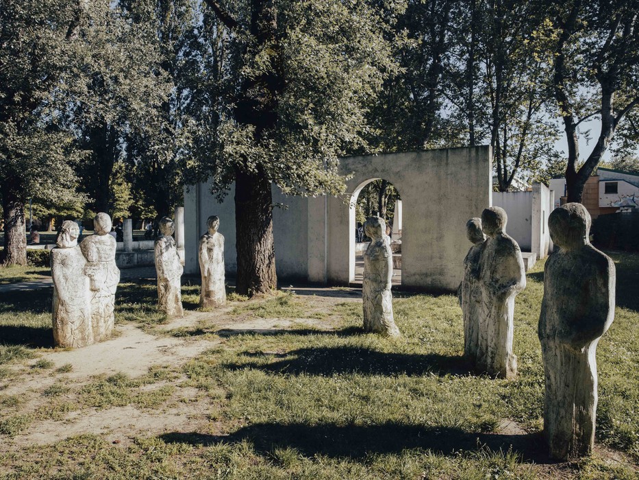 Monumento alla Resistenza, sculture di figure umane disposte in un'area verde con alberi e una struttura bianca sullo sfondo.