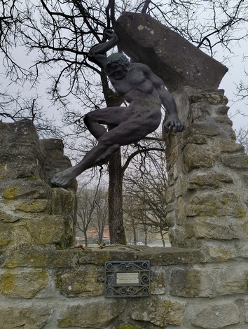 Monumento ai caduti di Botteghino di Zocca, con statua e struttura in pietra, immerso nel verde.