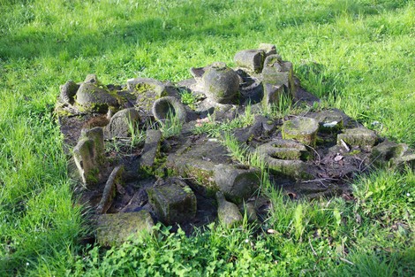 Monumento alla Resistenza in un prato, con resti di pietra mossi e circondati da erba verde.
