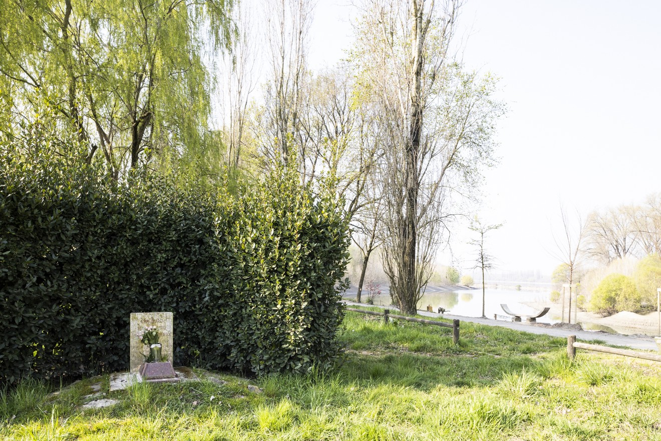 Cippo commemorativo immerso nella natura, vicino a un corso d'acqua e circondato da vegetazione.