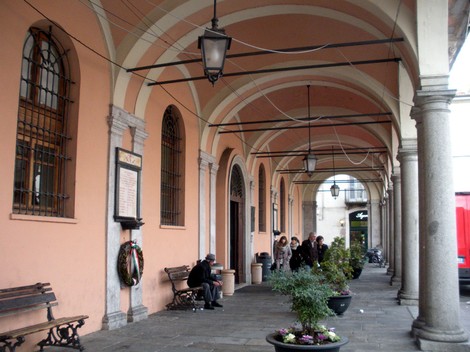 Lapide commemorativa ai caduti, situata sotto un portico a Castel San Giovanni, circondata da piante e visitatori.
