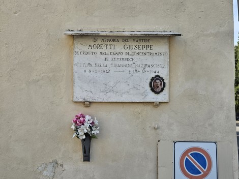Lapide marmorea su parete esterna, con iscrizione, ritratto ovale e vaso di fiori sottostante.