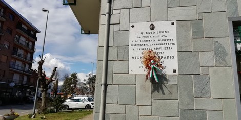 Lapide commemorativa con decorazioni floreali, situata su un edificio in un'area urbana.