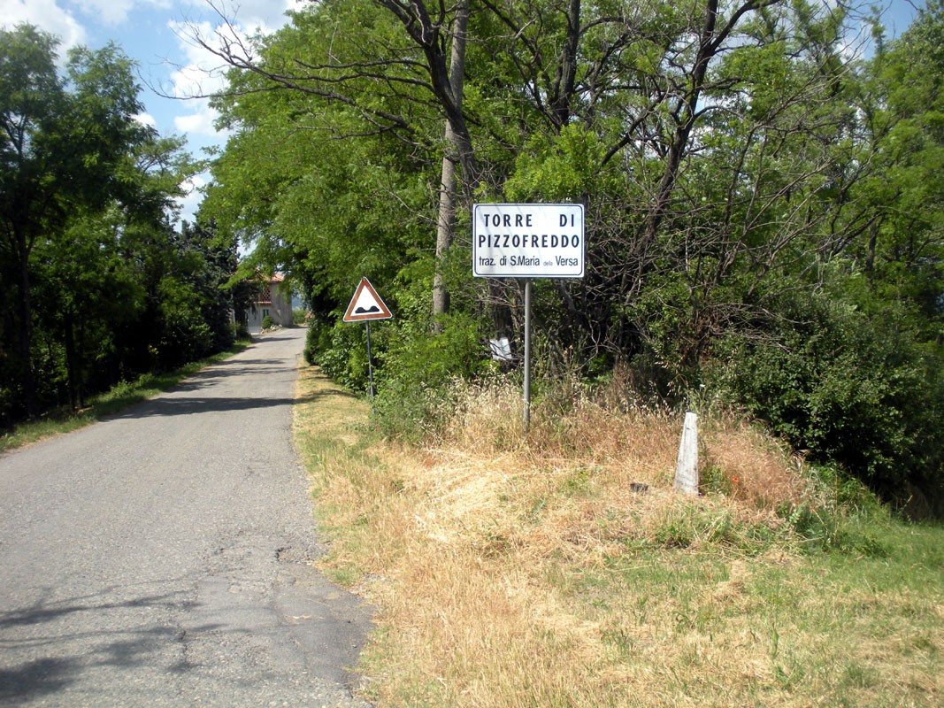 Cippo dedicato ad Achille, situato lungo una strada tranquilla immersa nella natura.