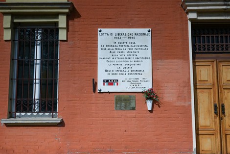 Lapide commemorativa della Lotta di Liberazione Nazionale, Casa Viaggi, con fiori ornamentali.
