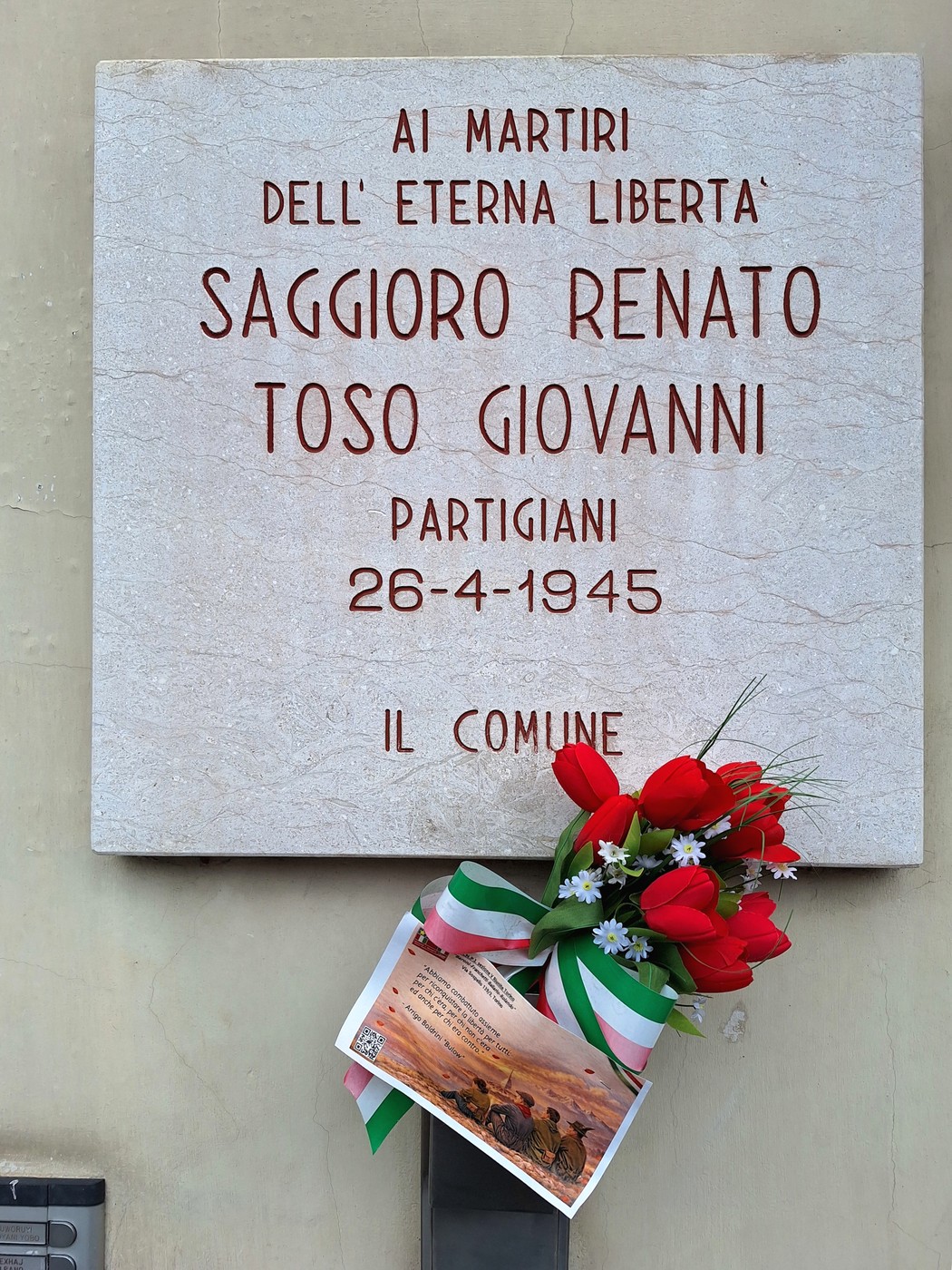 Lapide commemorativa in onore di Saggioro Renato e Toso Giovanni, con fiori e ornamenti tricolori.