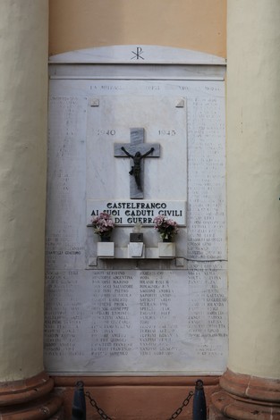 Lapide commemorativa dedicata ai caduti civili, con croce e fiori, in un contesto di rispetto e memoria.