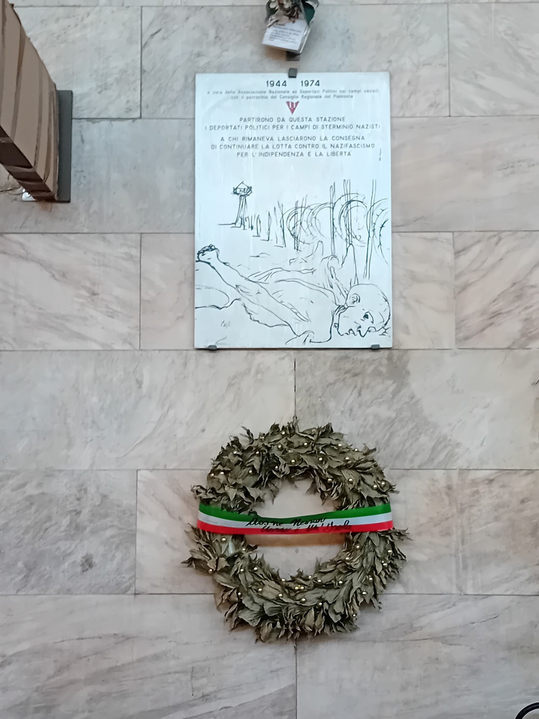 Lapide commemorativa ai deportati con una corona d'alloro ai piedi, simbolo di memoria e rispetto.