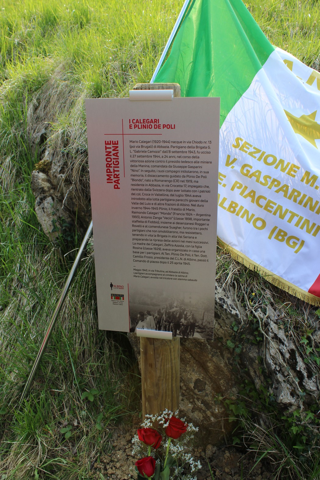 Impronta partigiana a Calegari e De Poli, con una targa commemorativa e fiori rossi vicino a una bandiera tricolore.