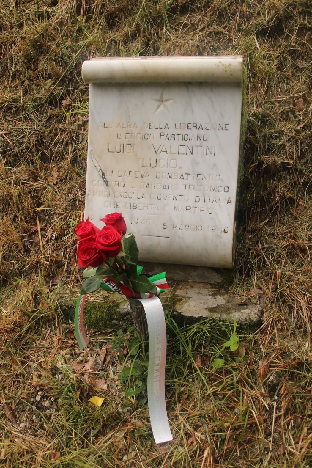 Lapide commemorativa dedicata a Luigi Valentini, partigiano, con fiori e nastri celebrativi.
