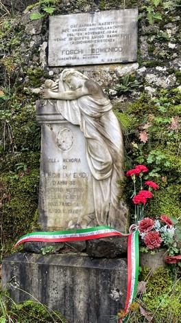 Monumento a Foschi con statua e lapide commemorativa, arricchito da fiori e nastri tricolori.