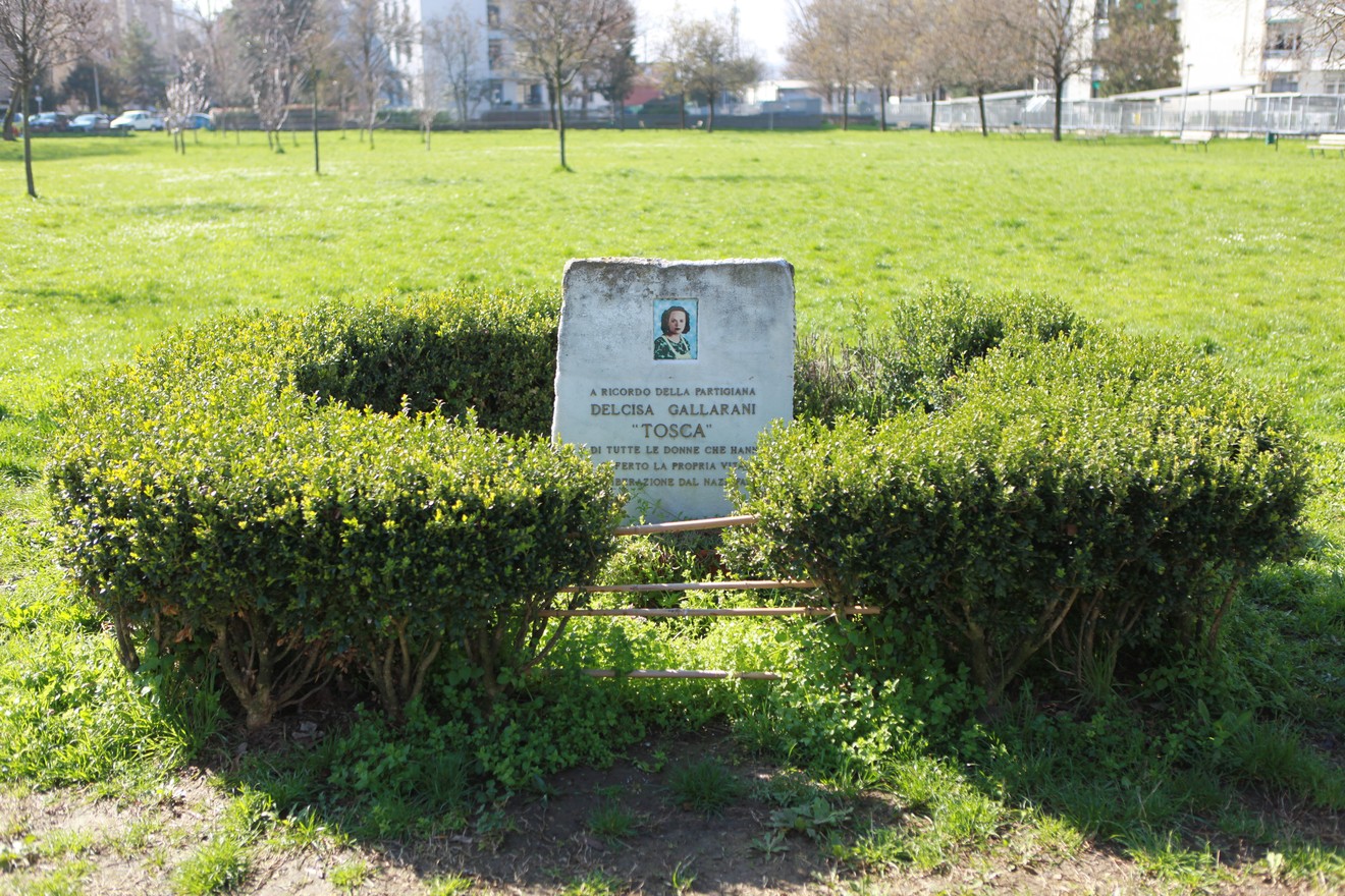 Cippo commemorativo in un parco, circondato da cespugli ben curati e verde erba.