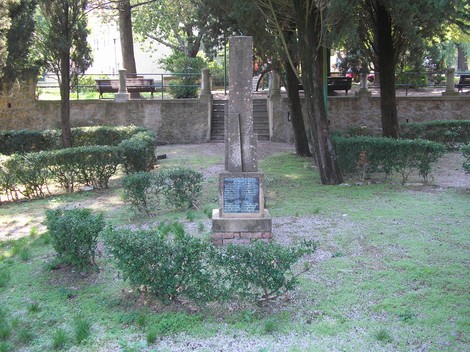 Monumento ai caduti immerso nel verde, circondato da alberi e cespugli, in un'atmosfera di commemorazione.