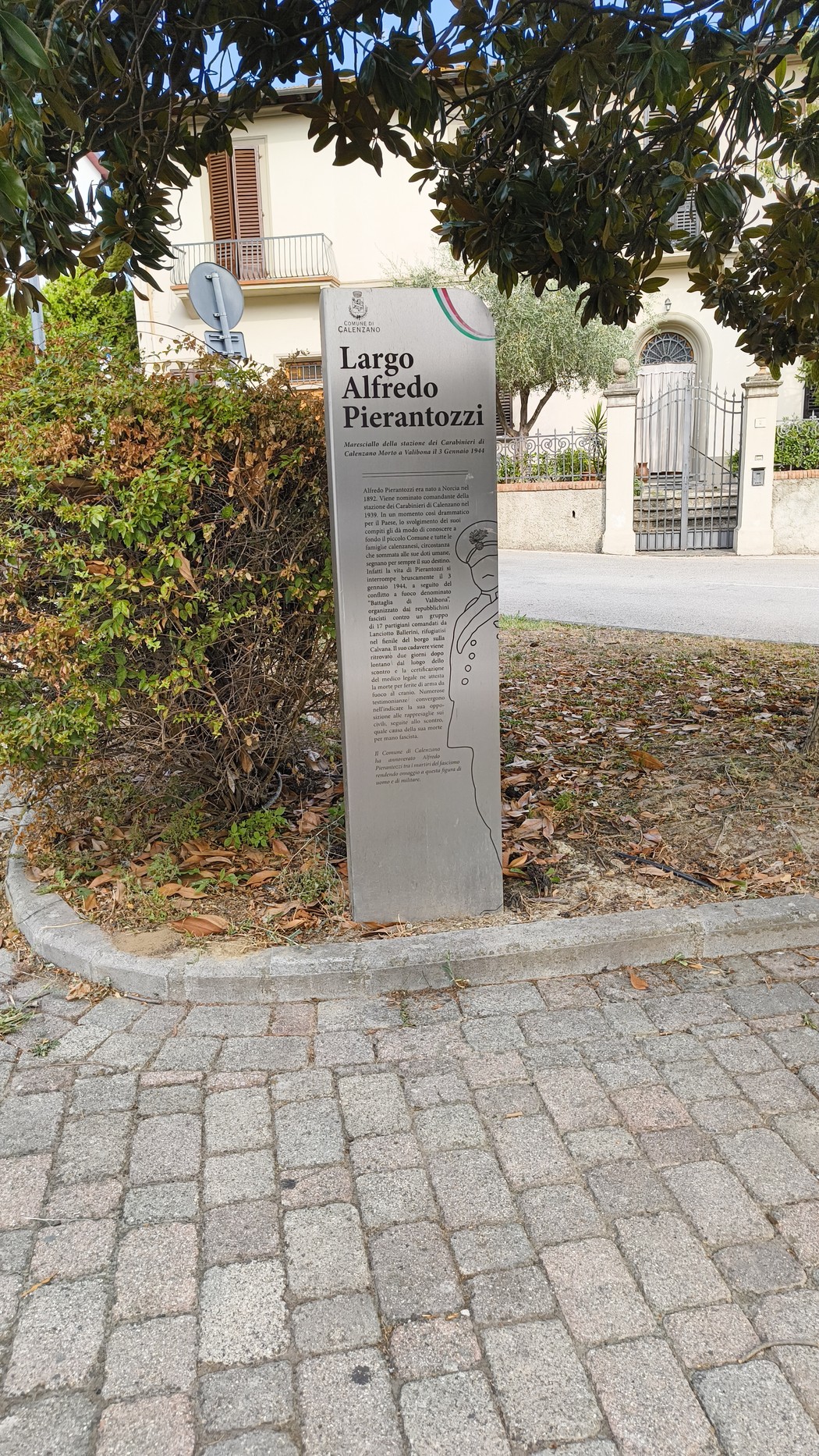 Stele informativa dedicata a Alfredo Pierantozzi in Largo a lui intitolato, circondata da vegetazione.