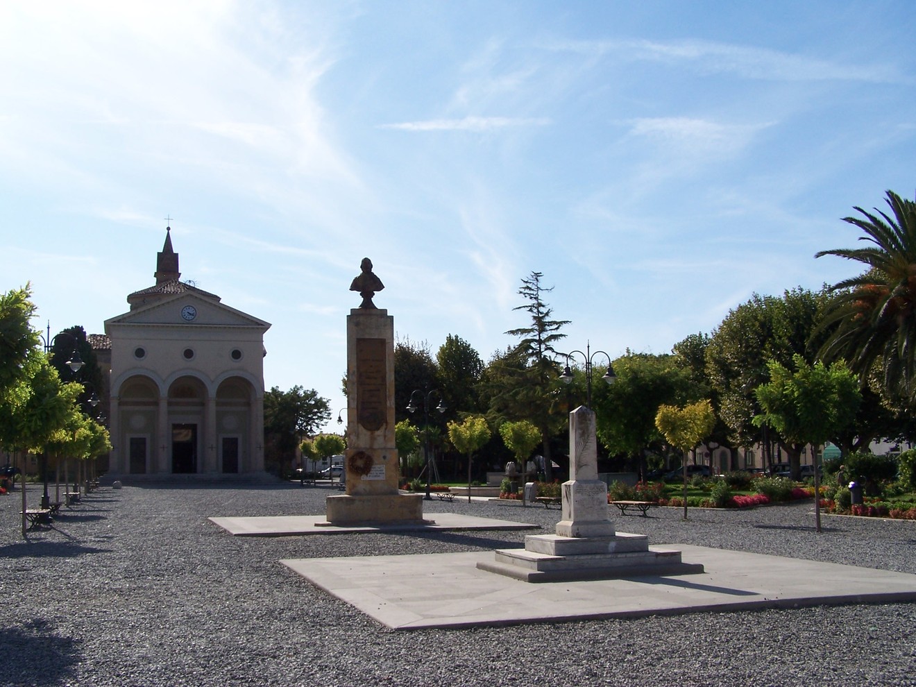 Cippo di Vada, monumento circondato da un giardino, con una chiesa sullo sfondo e alberi ornamentali.