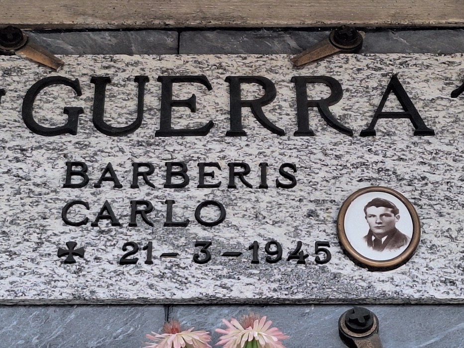 Lapide in marmo con scritta "Guerra", iscrizione e ritratto fotografico ovale di un giovane.