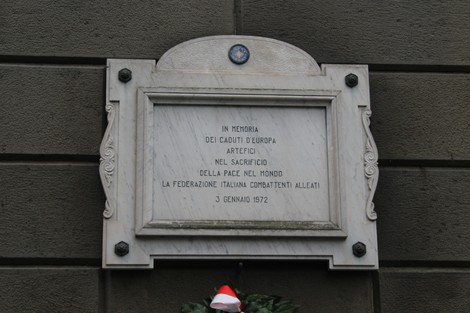 Lapide commemorativa dedicata agli Alleati caduti, situata in una parete esterna, con decorazioni floreali.