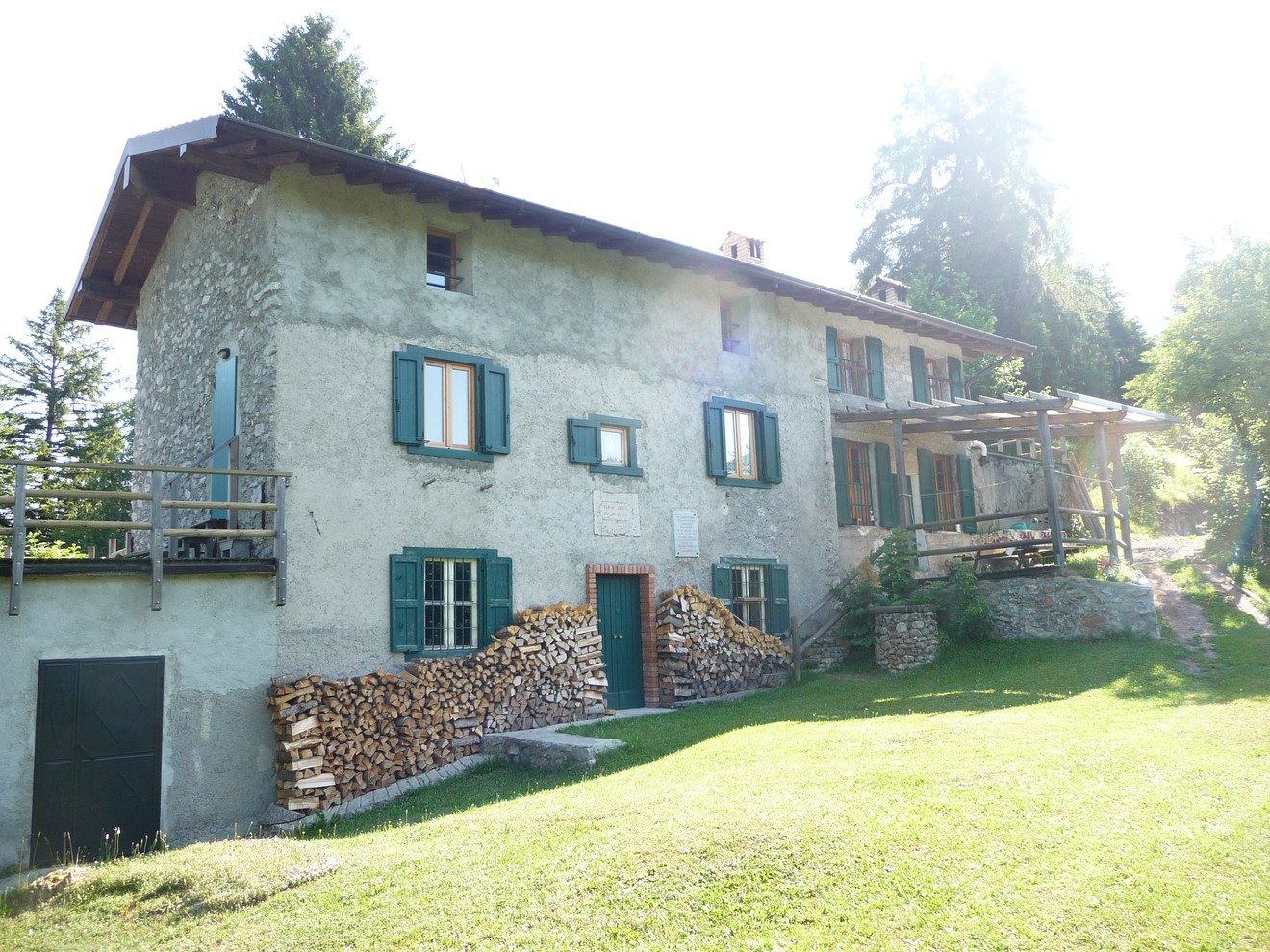 Edificio rustico con finestre verdi e legna accatastata, situato nella natura all'aperto.