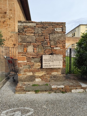 Lastra commemorativa in pietra dedicata alle vittime dei bombardamenti di Pisa, situata accanto a un edificio.