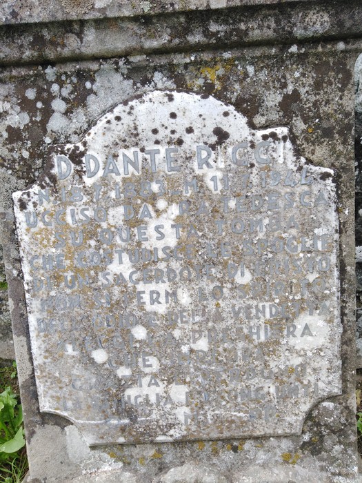 Tomba di Ricci, stele in pietra con iscrizione parzialmente scolorita, circondata da erba e vegetazione.