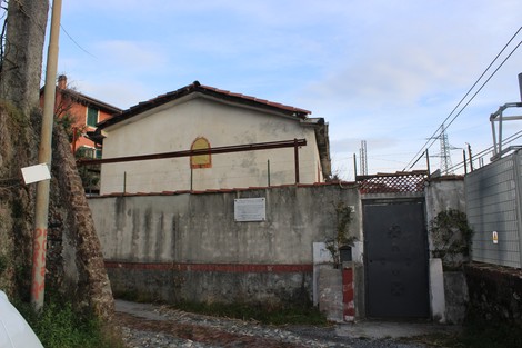 Lapide familiari Pirc su un muro, contesto urbano con edifici e recinzioni visibili.